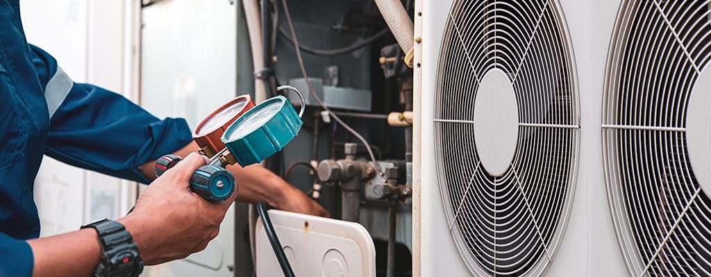 Commercial HVAC system service technician using measuring manifold gauge checking refrigerant and filling industrial air conditioner