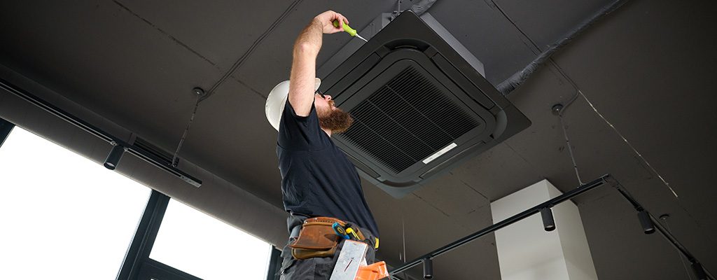 hvac technician standing on ladder installing air conditioner at the office